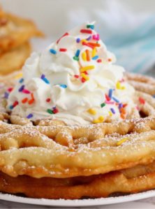 stack of funnel cakes with whipped cream and sprinkles