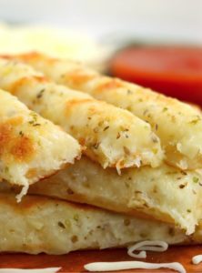cheesy breadsticks in front of bowls of dipping sauce