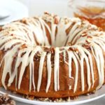 glazed rum cake on a white plate surrounded by crushed pecans