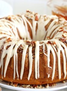 glazed rum cake on a white plate surrounded by crushed pecans