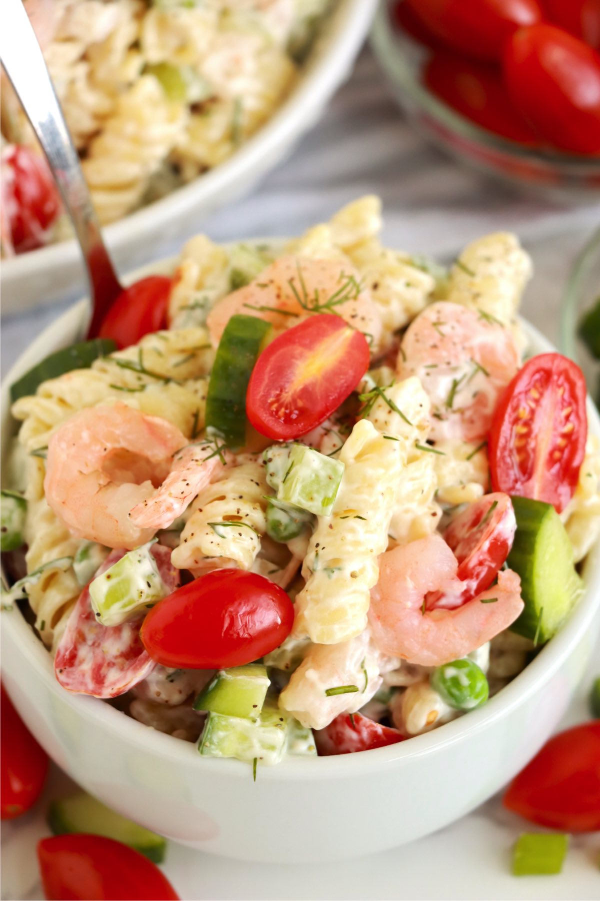 spoon in a bowl of pasta salad with tomatoes and shrimp