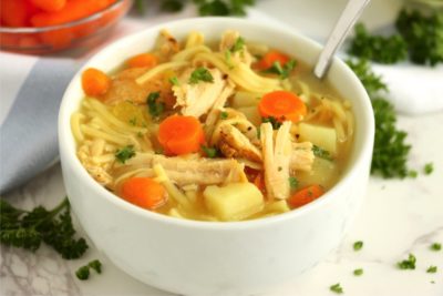 A bowl of soup filled with carrots, potatoes and turkey