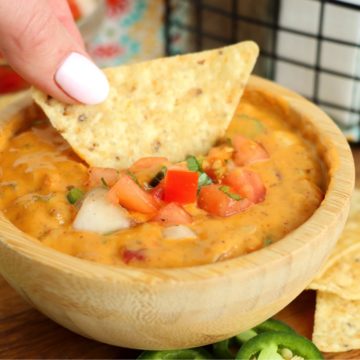 dipping a chip into a small wooden bowl of chili con queso