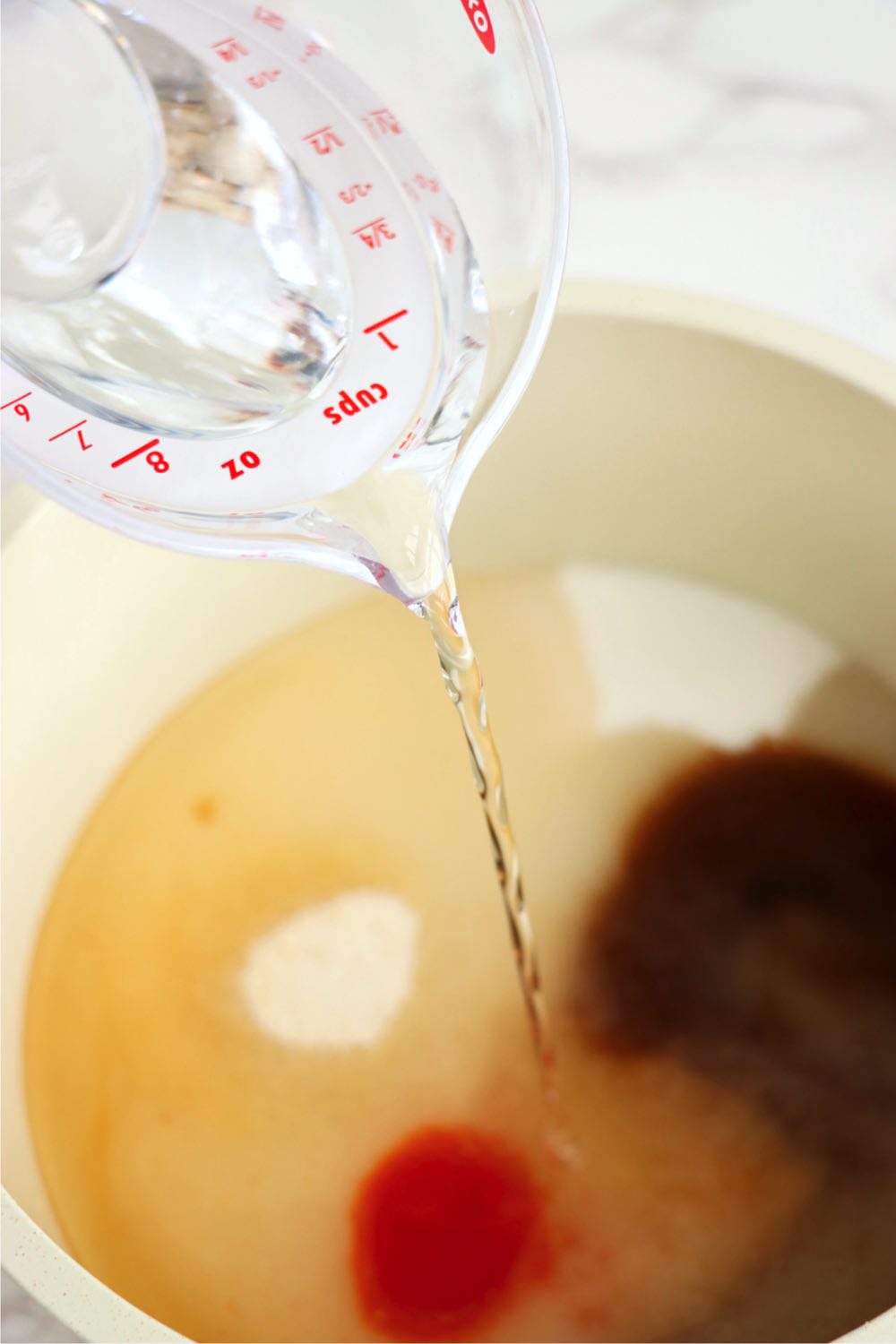 Pouring vinegar from a measuring cup into a bowl filled with sugar, Worcestershire sauce and other ingredients