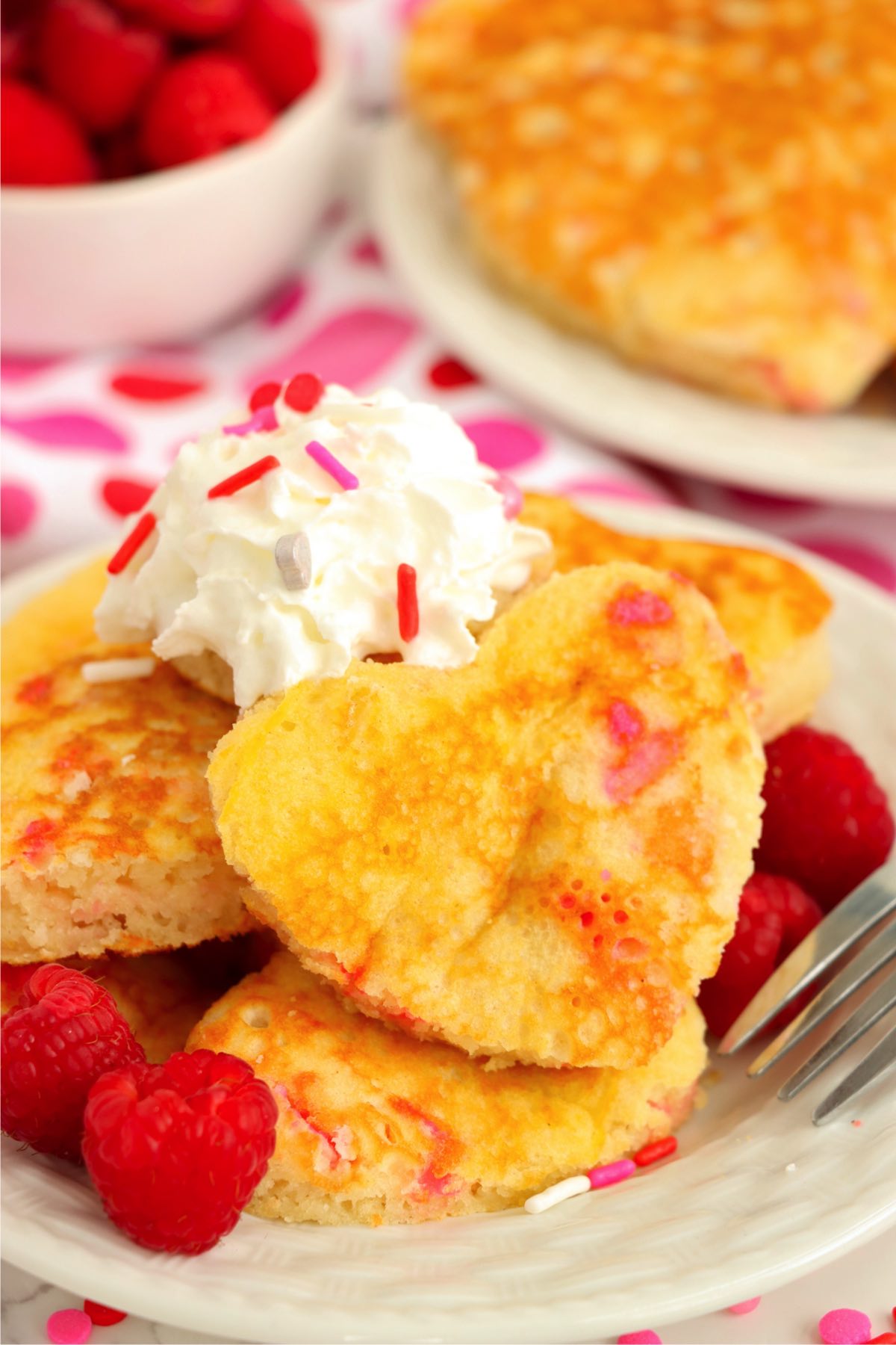 Heart-shaped pancakes filled with sprinkles with raspberries on the side