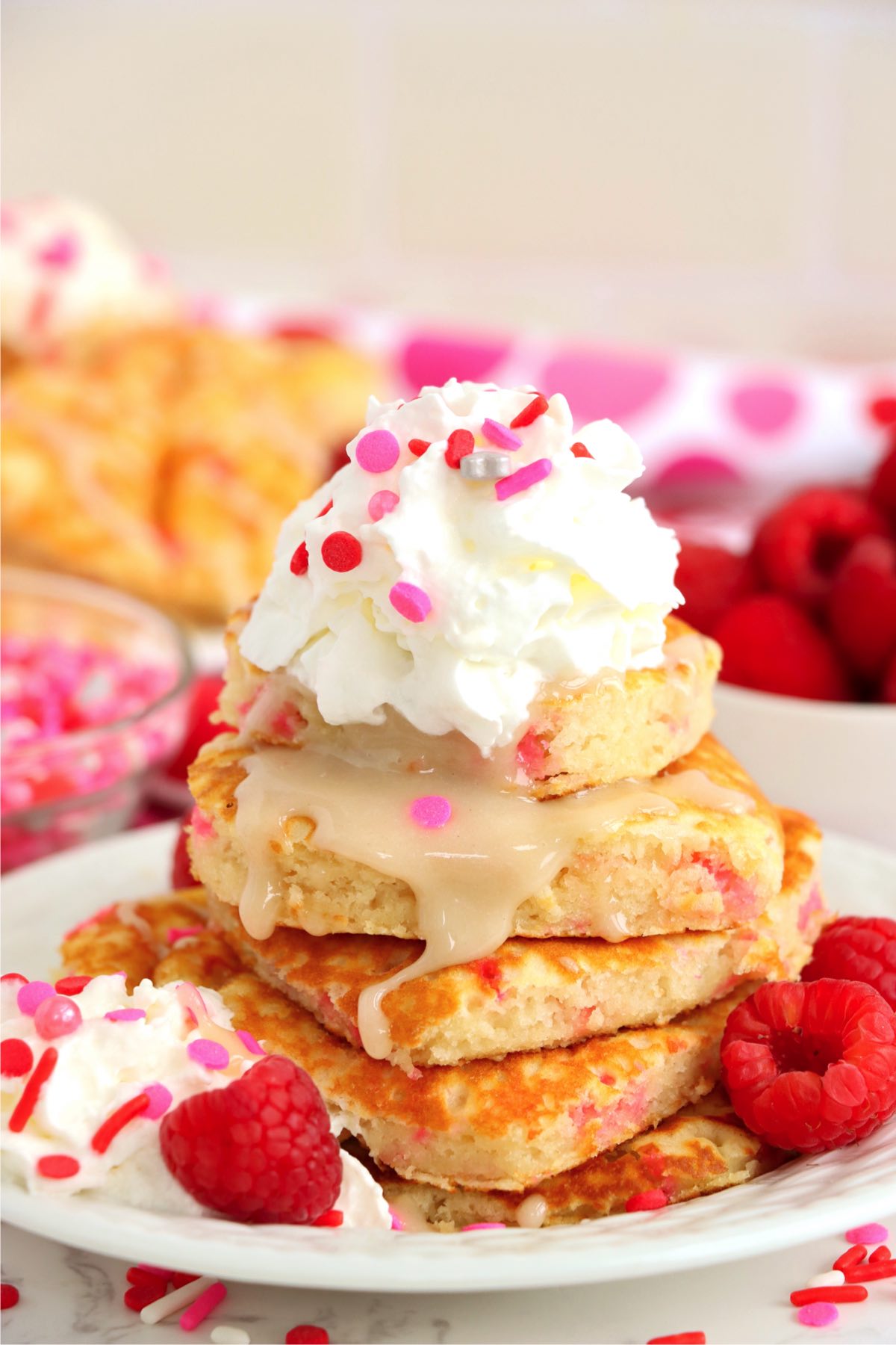 stack of pancakes topped with glaze, whipped cream and sprinkles
