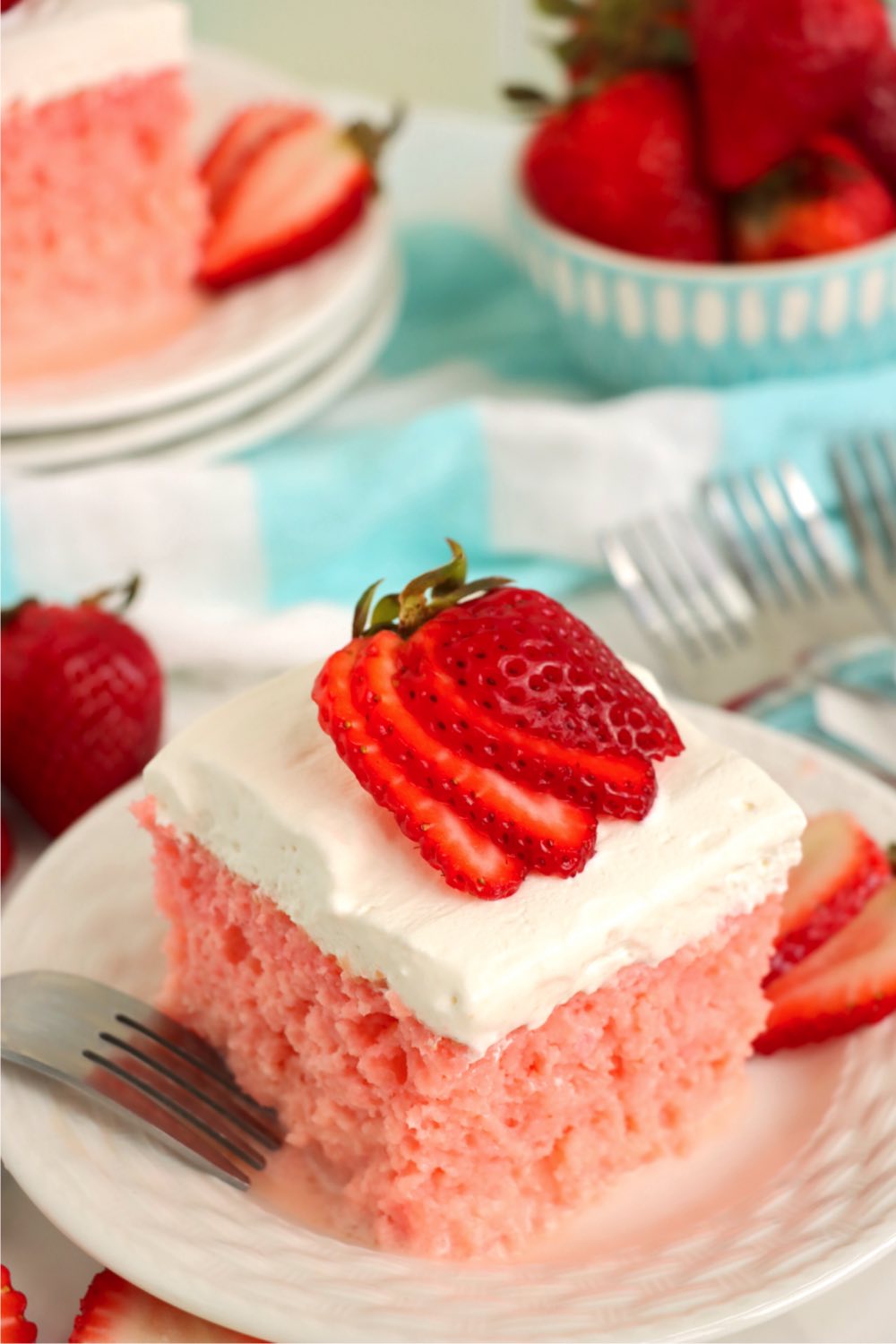 piece of strawberry tres leches cake on a white dessert plate with strawberries in background