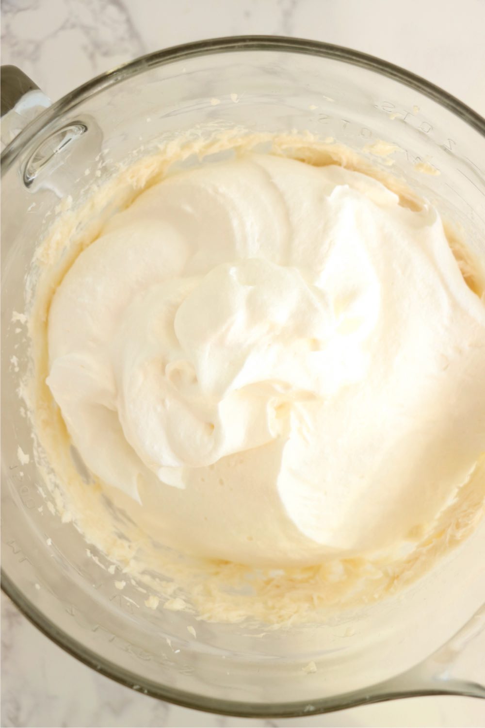 Whipped topping added to cream cheese mixture in a glass bowl