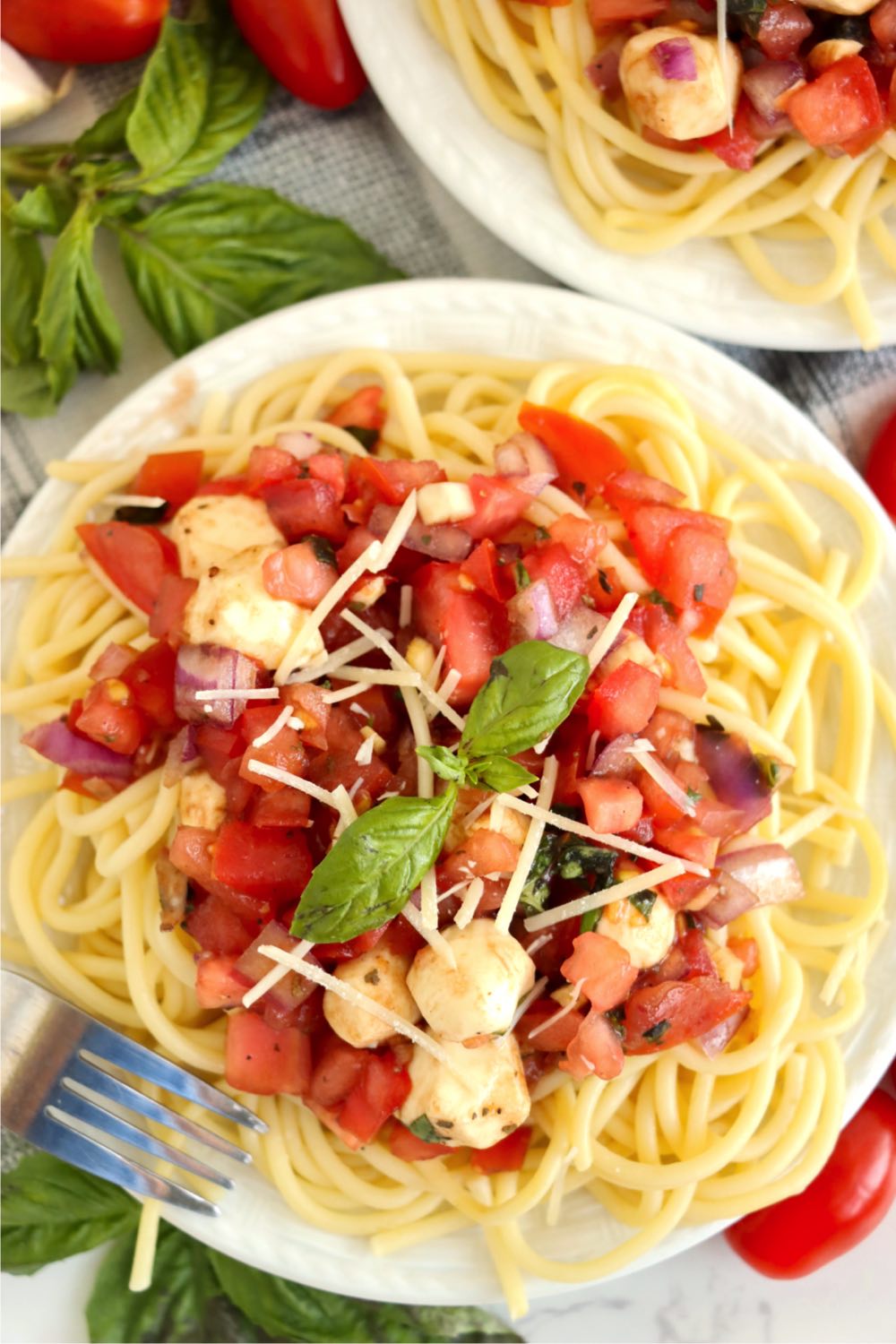 A plate of bruschetta pasta salad garnished with basil and parmesan cheese.