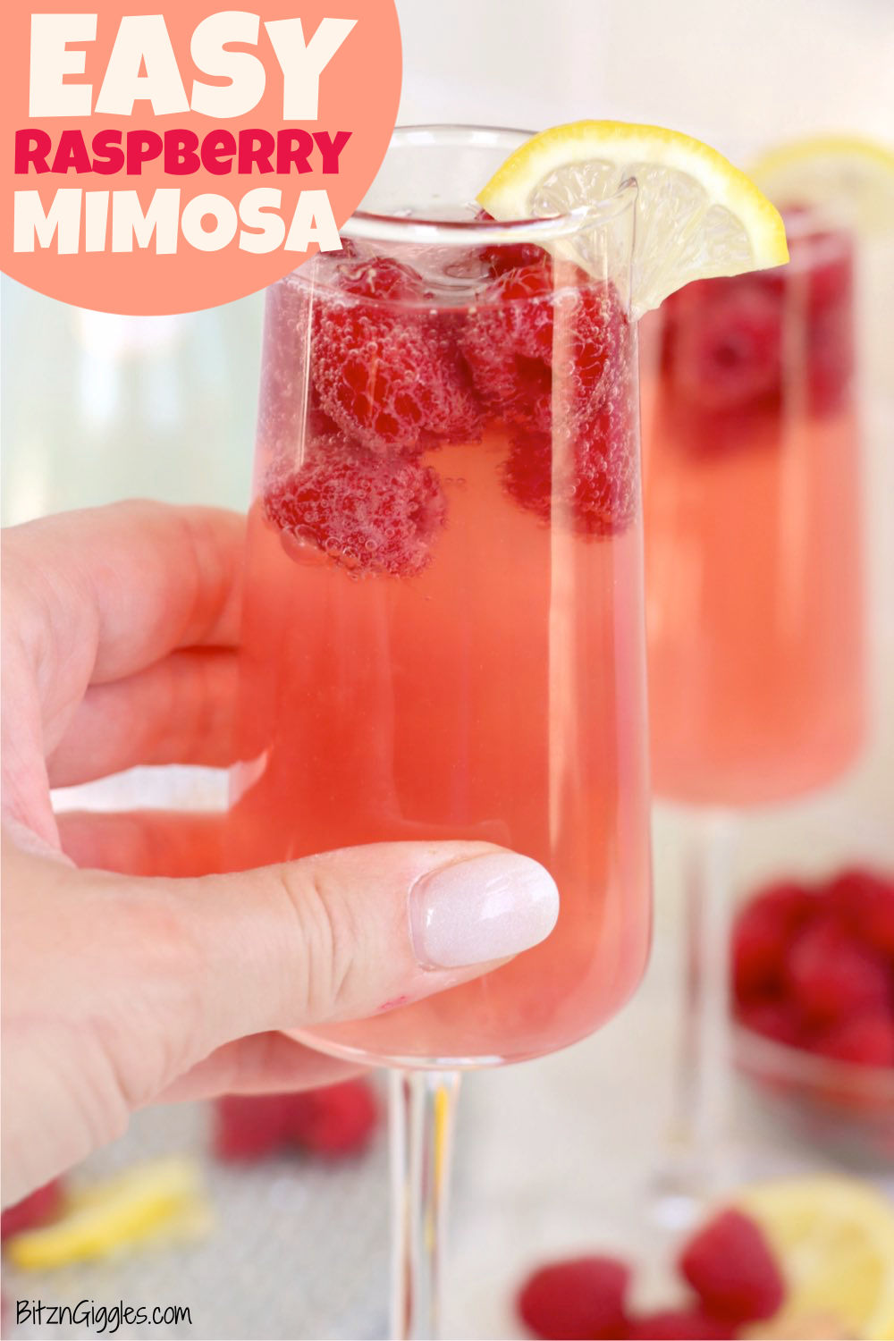 hand holding a flute glass of raspberry mimosa with raspberries and a lemon as garnish.
