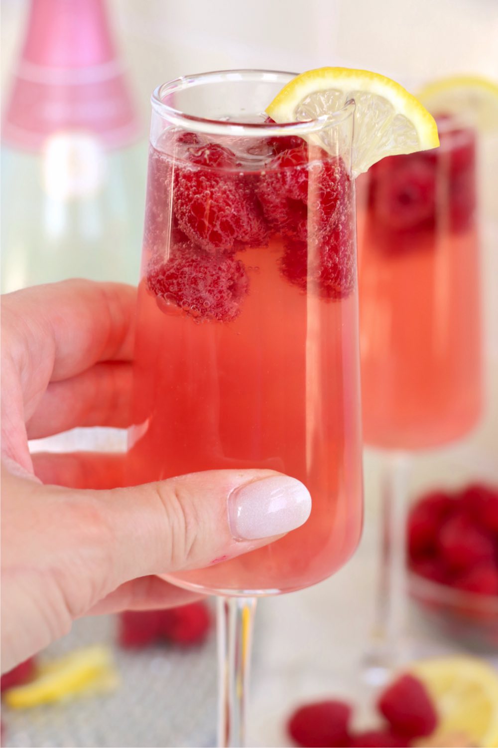 hand holding a cocktail garnished with fresh raspberries.