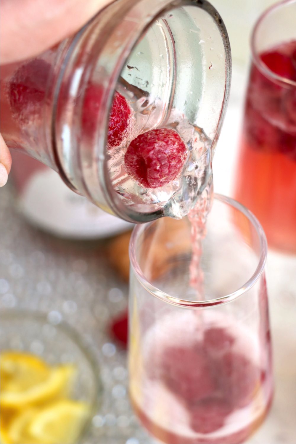 pouring a fresh raspberry mimosa cocktail into a champagne glass