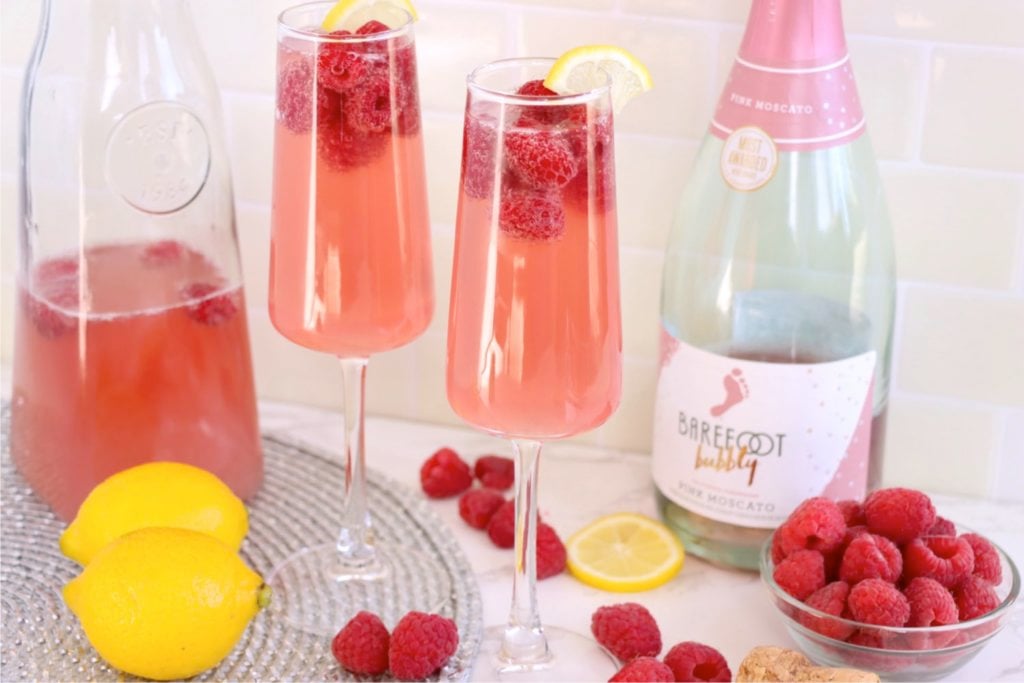 Two glasses of raspberry mimosa with raspberries and lemons.