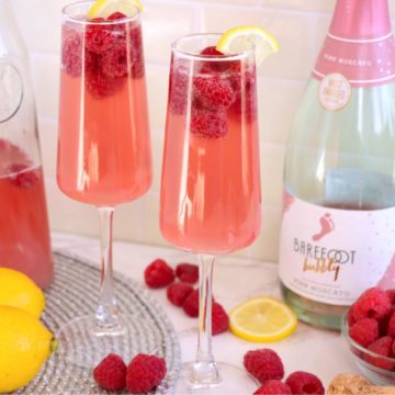 Two glasses of raspberry mimosa with raspberries and lemons.