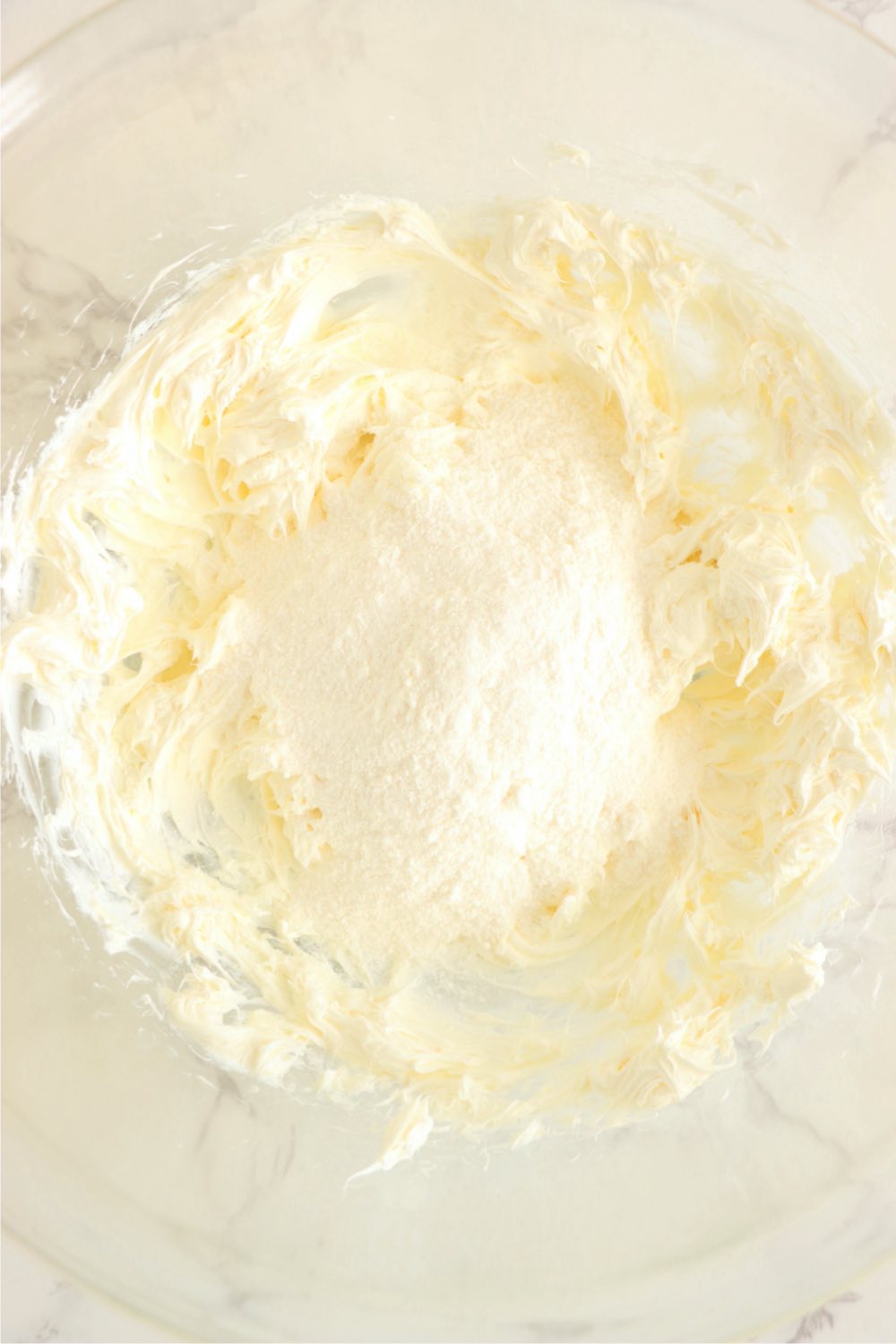 Banana pudding mix on top of whipped cream cheese in a mixing bowl.