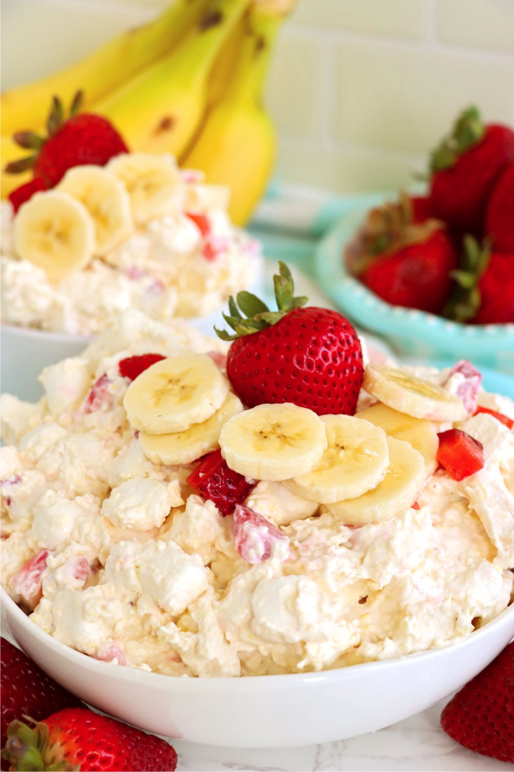 white bowl filled with a fruit fluff salad and garnished with fresh strawberries and sliced bananas.