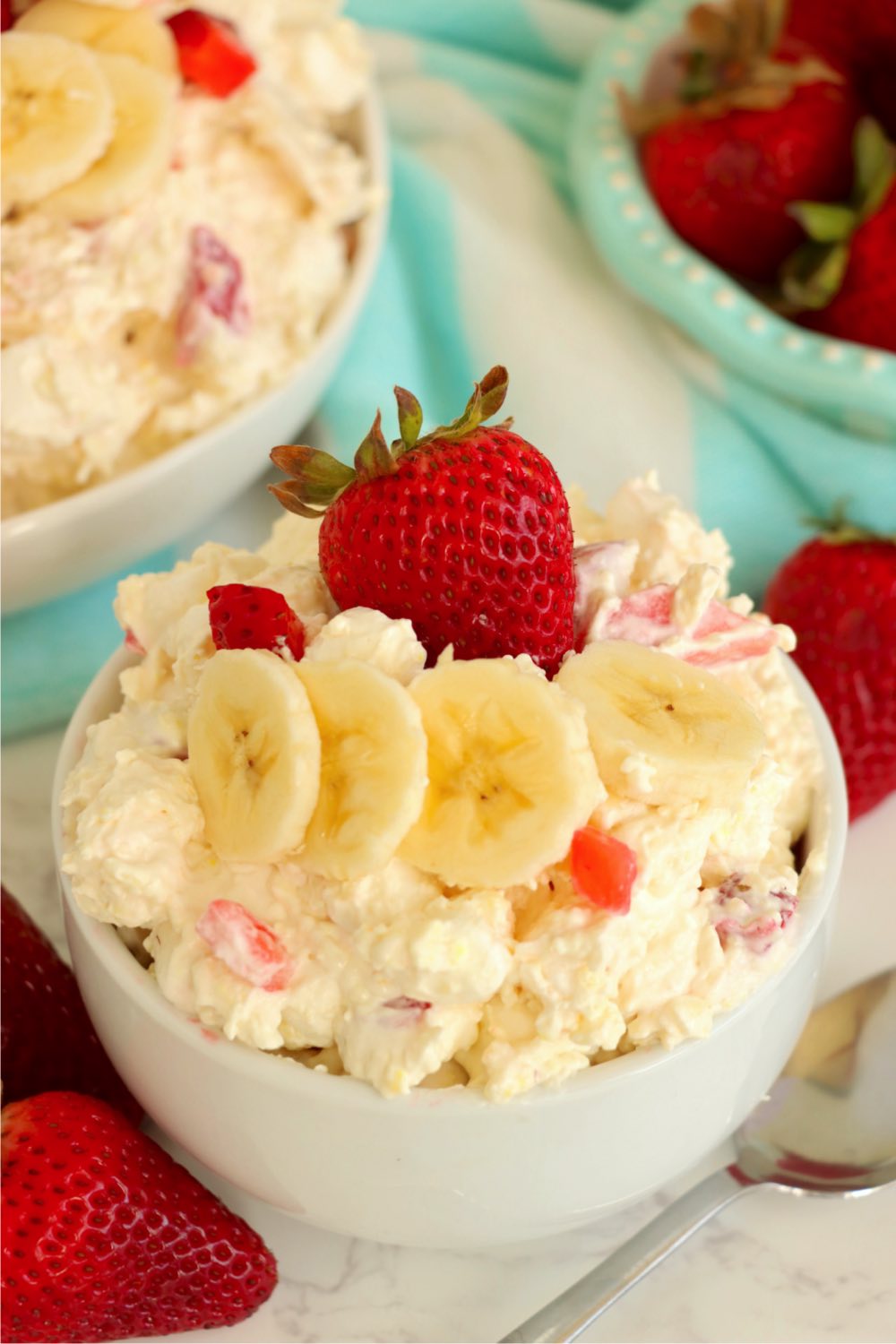 white bowl filled with a fluff salad garnished with fresh bananas and strawberries.