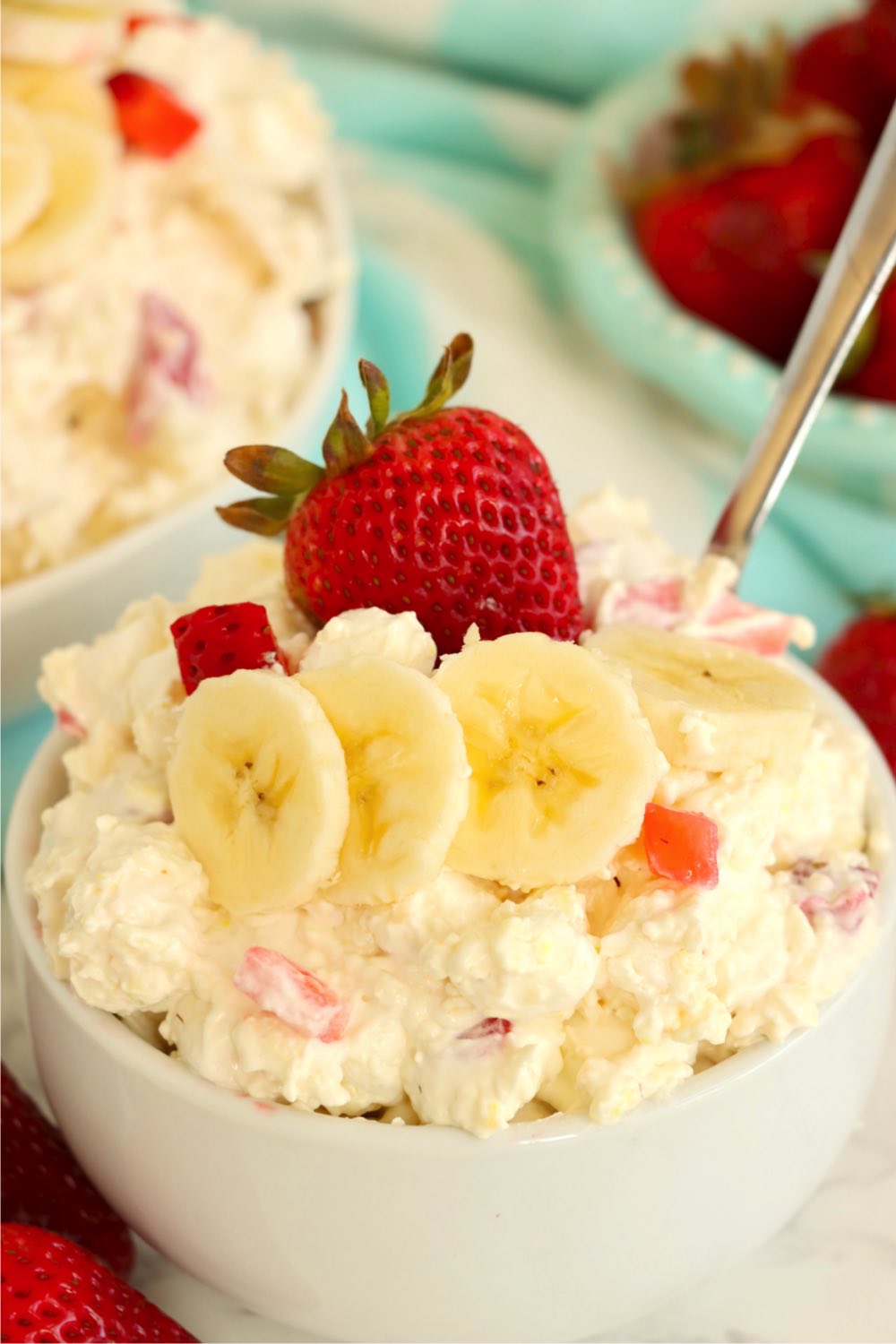 A white bowl filled with a fluff salad and garnished with bananas and a strawberry.