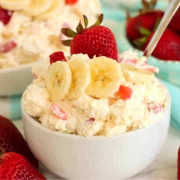 white bowl with a spoon holding a strawberry and banana dessert salad.