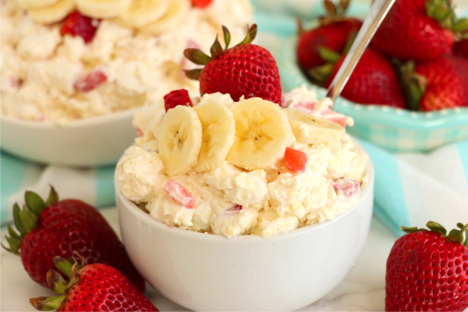 white bowl with a spoon holding a strawberry and banana dessert salad.