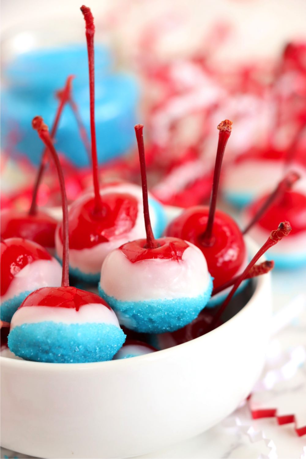 Small white bowl holding cherries dipped in white chocolate and blue sprinkles.