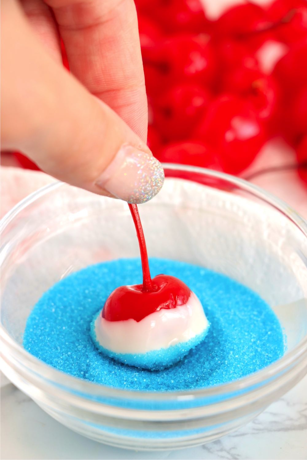Dipping a white chocolate covered cherry into blue sprinkles.
