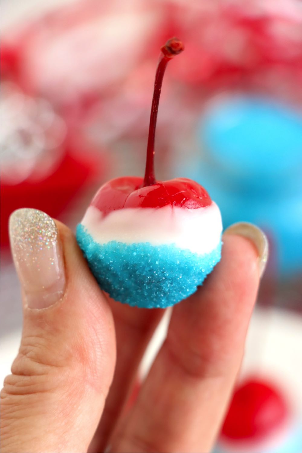 Fingers holding a red, white and blue cherry with stem.