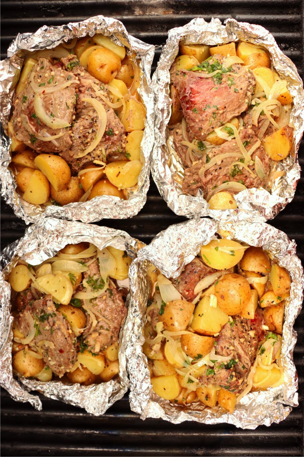 Four foil packs filled with steak and potatoes.