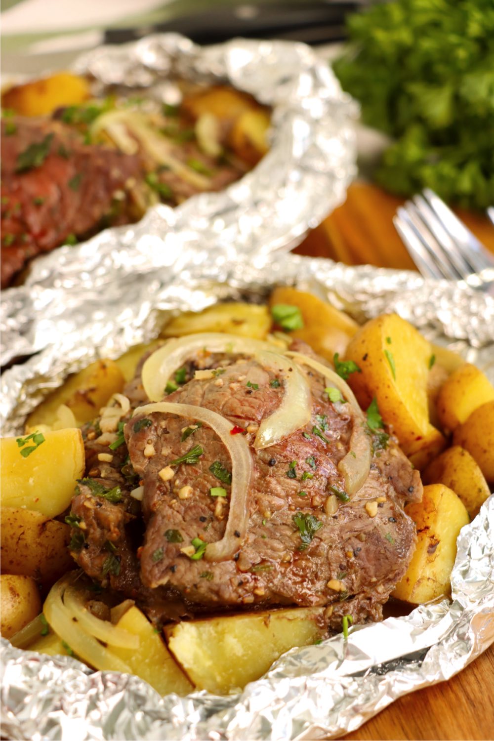 Onion topped steak and potatoes in an aluminum foil packet.