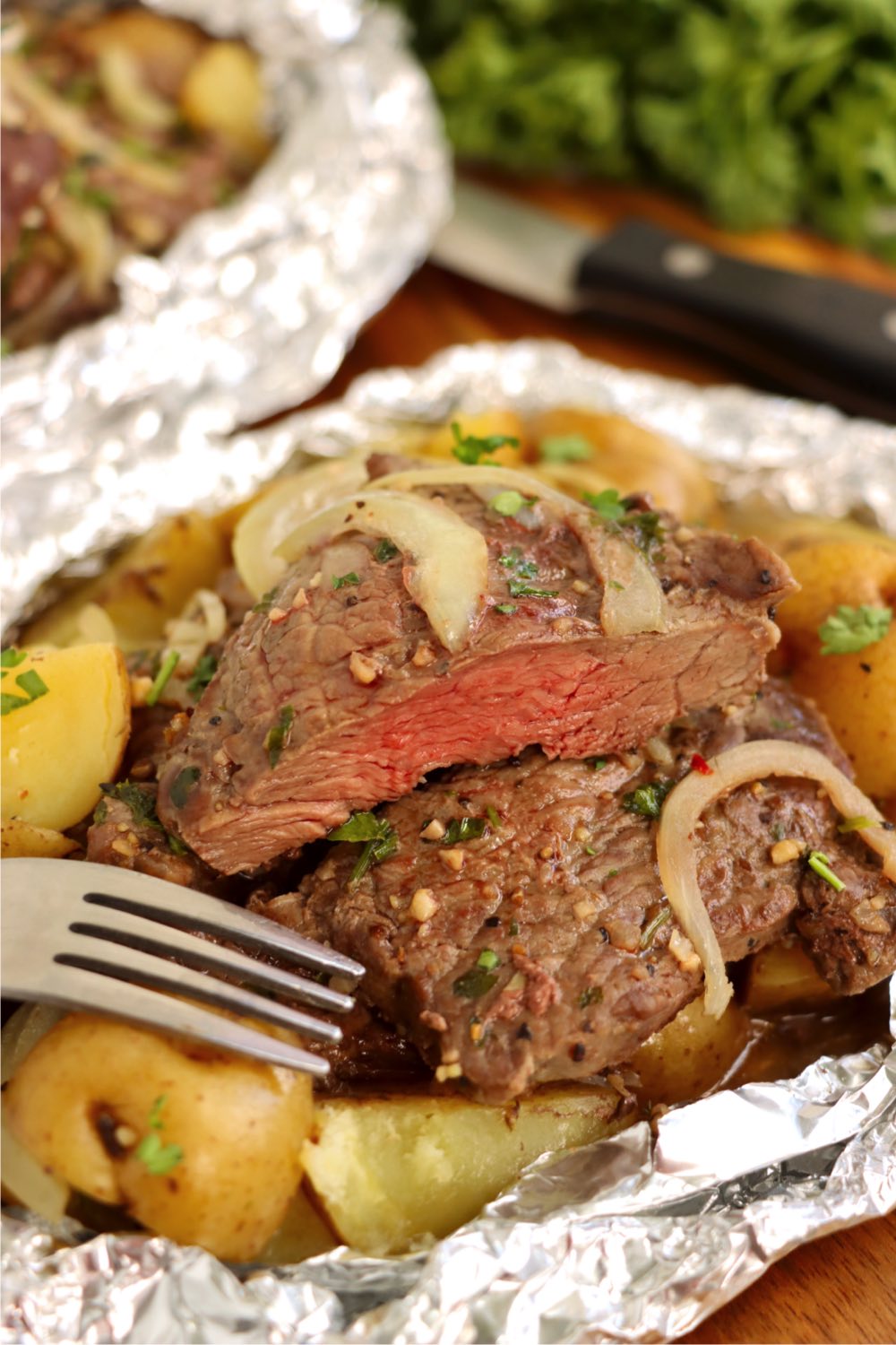 Steak cut in half in a foil packet with potatoes.