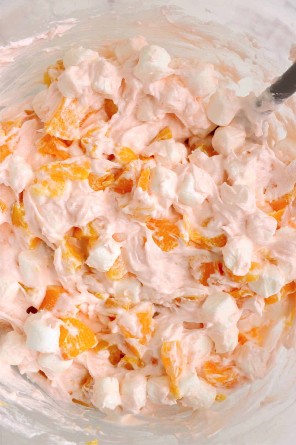Mixing mini marshmallows and peaches into a creamy fluff salad.