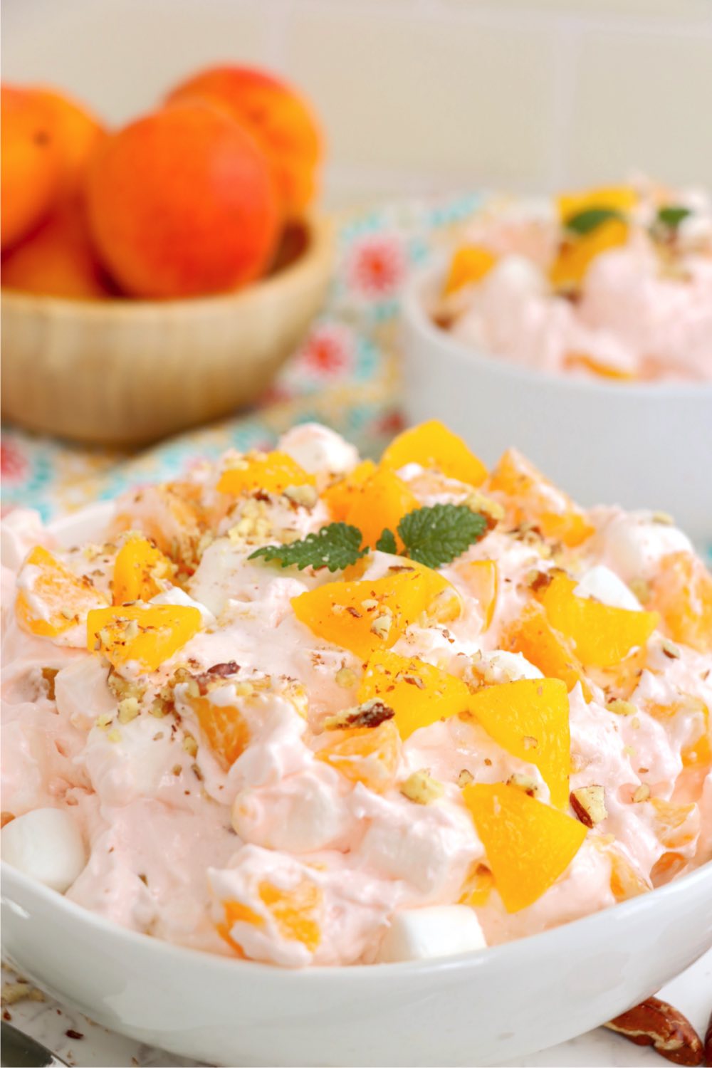 Fluffy jello salad in a bowl garnished with peaches and a mint leaf.