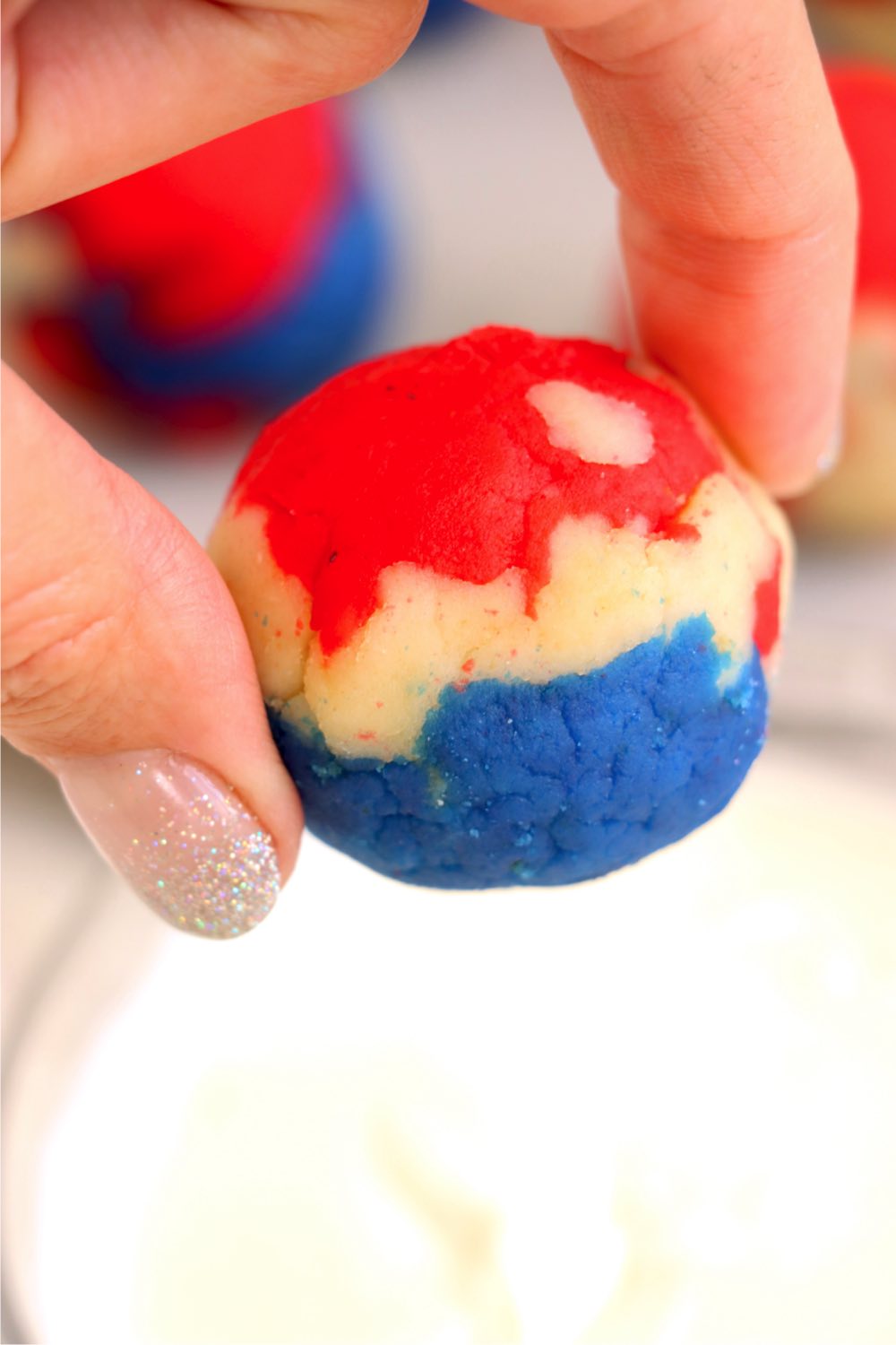 Fingers holding a red, white and blue cake ball.