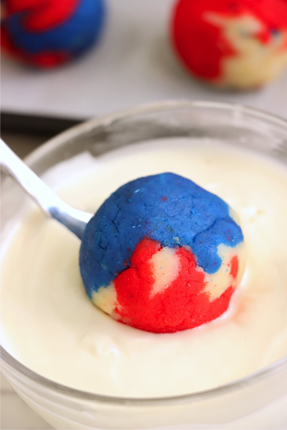 Dipping a red, white and blue cake ball into white frosting with a spoon.