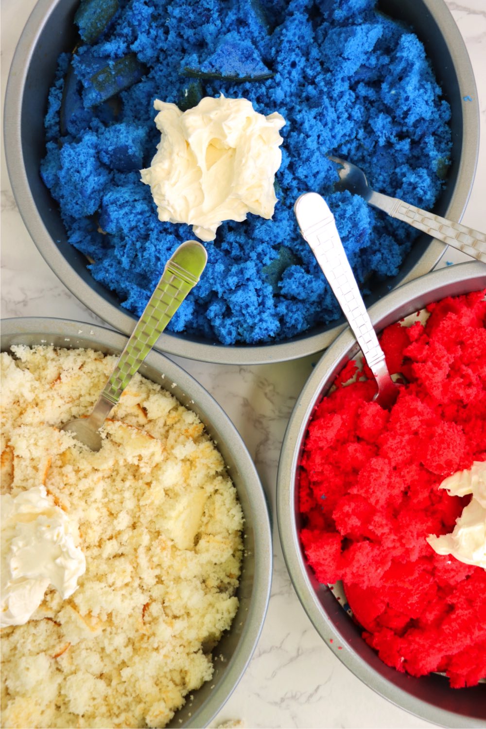 Three cake pans of crumbled red, white and blue cake with dollops of cream cheese on top.