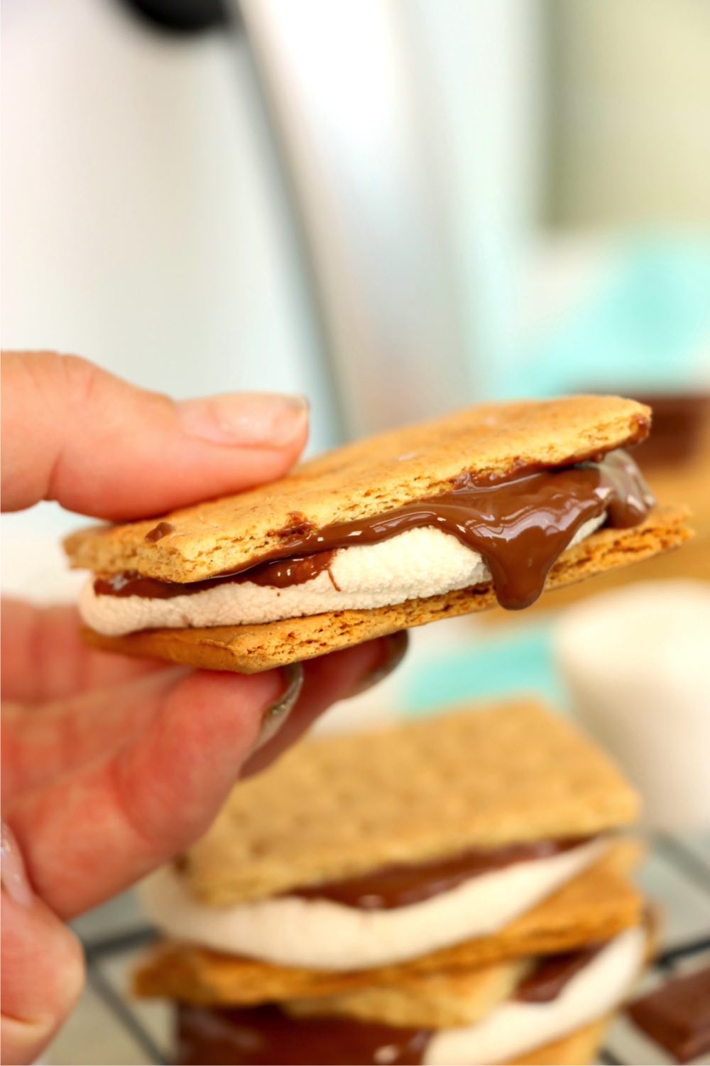 Hand holding a s'more in front of an air fryer.