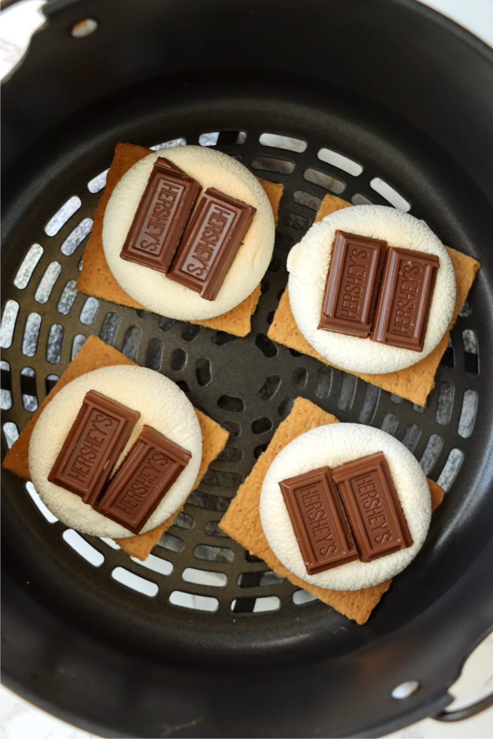 Stacks of graham crackers, marshmallows and chocolate pieces in an air fryer basket.