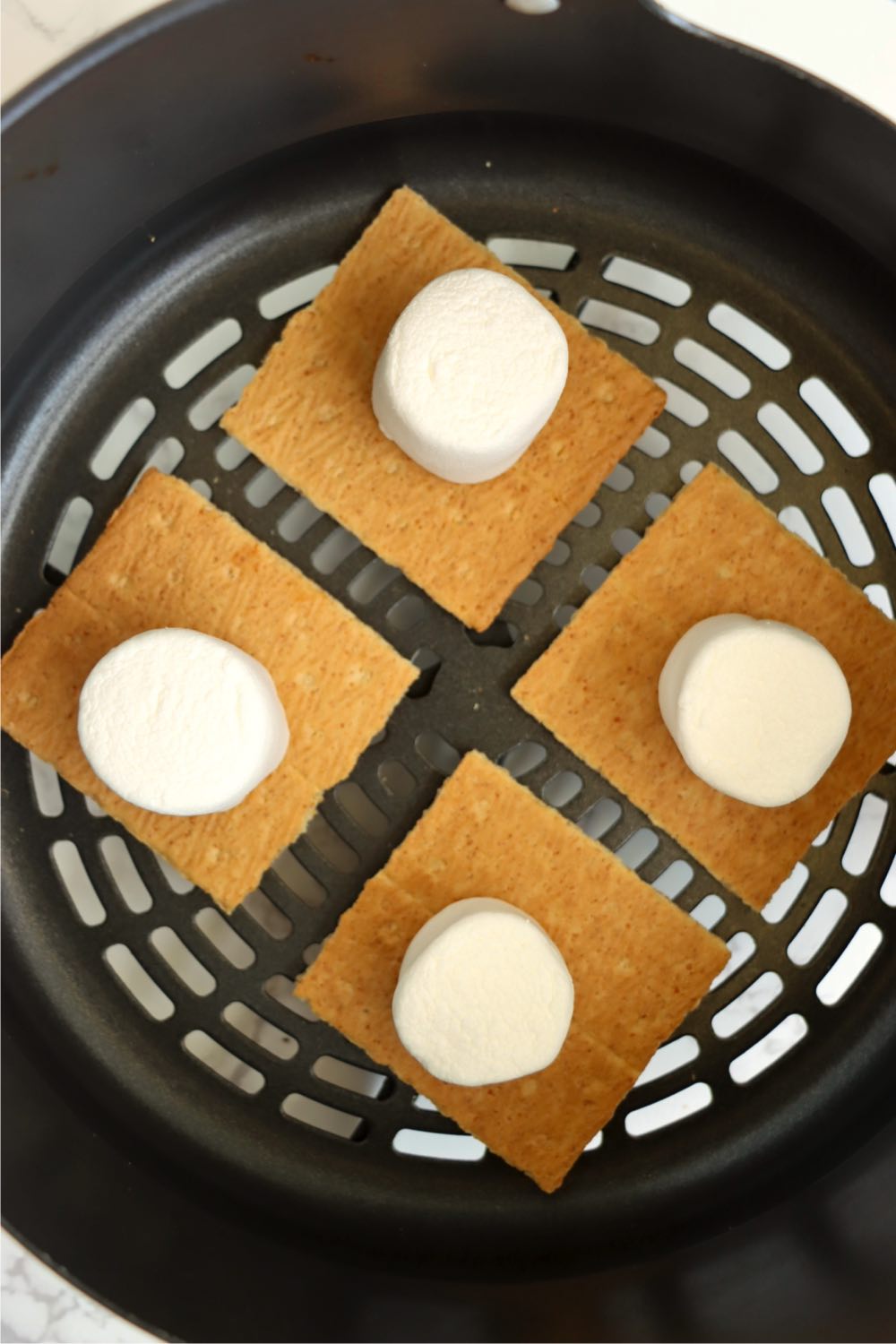 Marshmallows on top of graham crackers in air fryer basket.