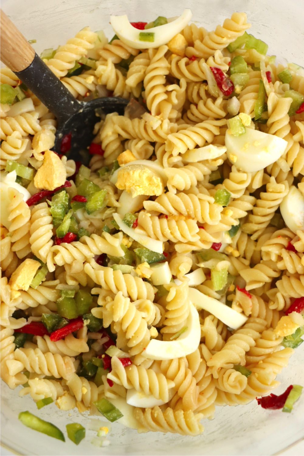 A bowl filled with pasta, chopped eggs, celery, onion, pimentos, green peppers, and sweet relish.