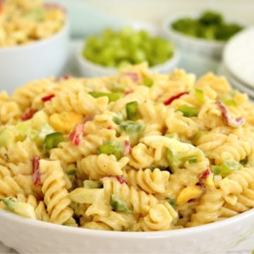 White serving bowl filled with a creamy rotini pasta salad with bowls of ingredients in the background.