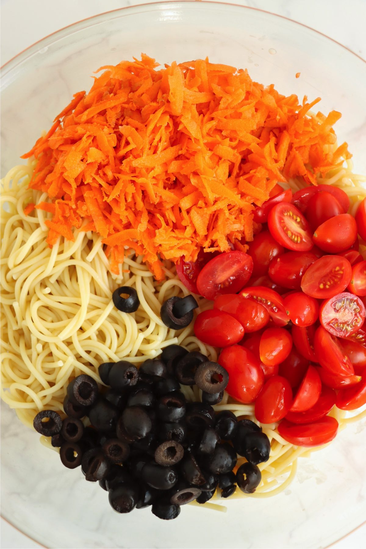 Bowl filled with angel hair pasta, carrots, tomatoes and olives.