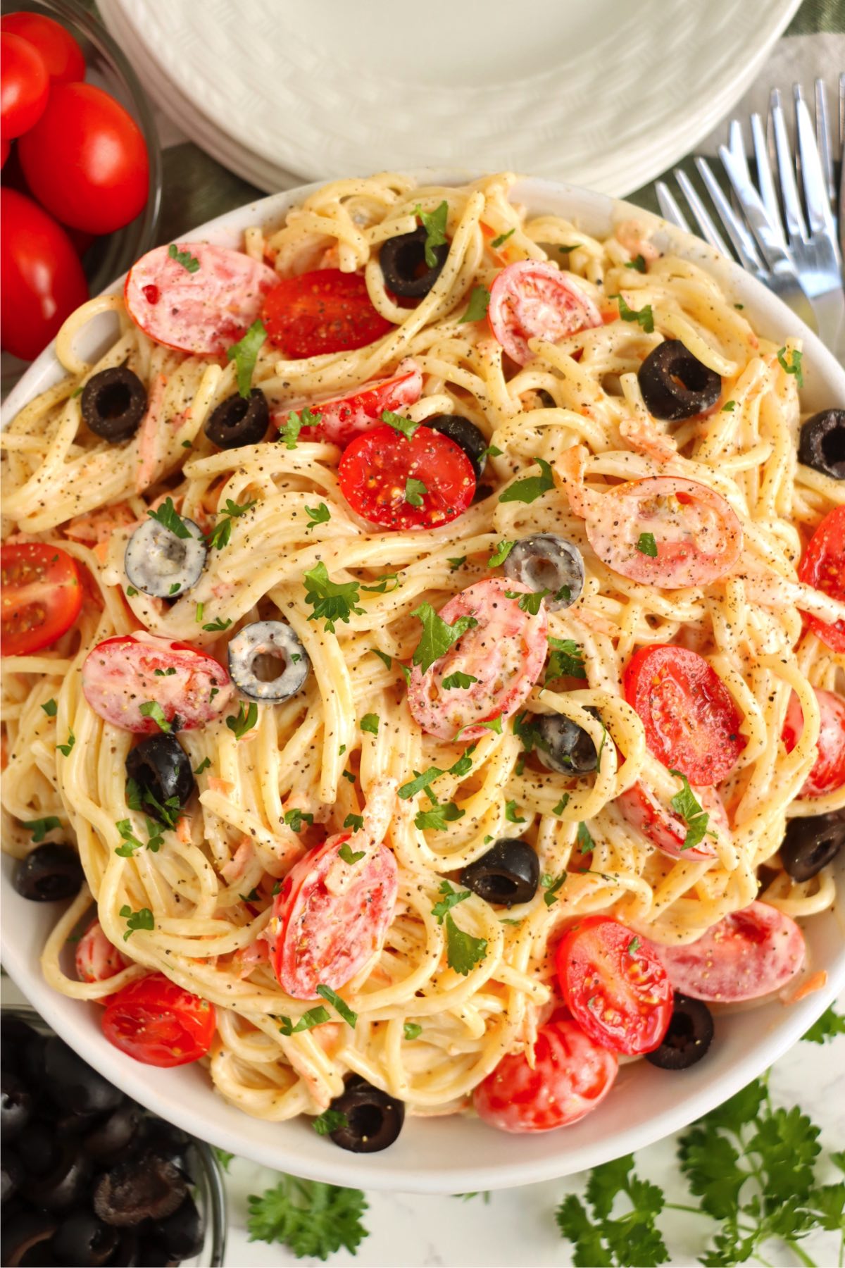 Large bowl of angel hair pasta tossed with a creamy italian dressing and garnished with tomatoes, carrots and black olives.