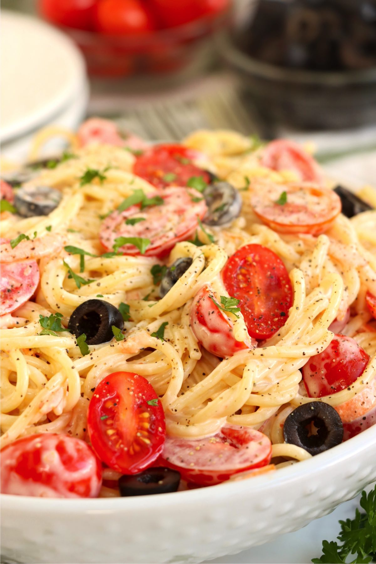 Heaping bowl of creamy angel hair pasta salad filled with black olives and tomatoes.