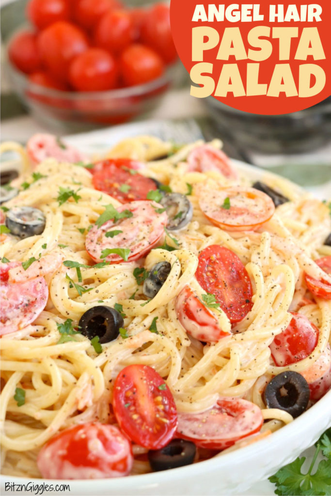 Creamy angel hair pasta salad with cherry tomatoes and sliced black olives in a big white serving bowl.