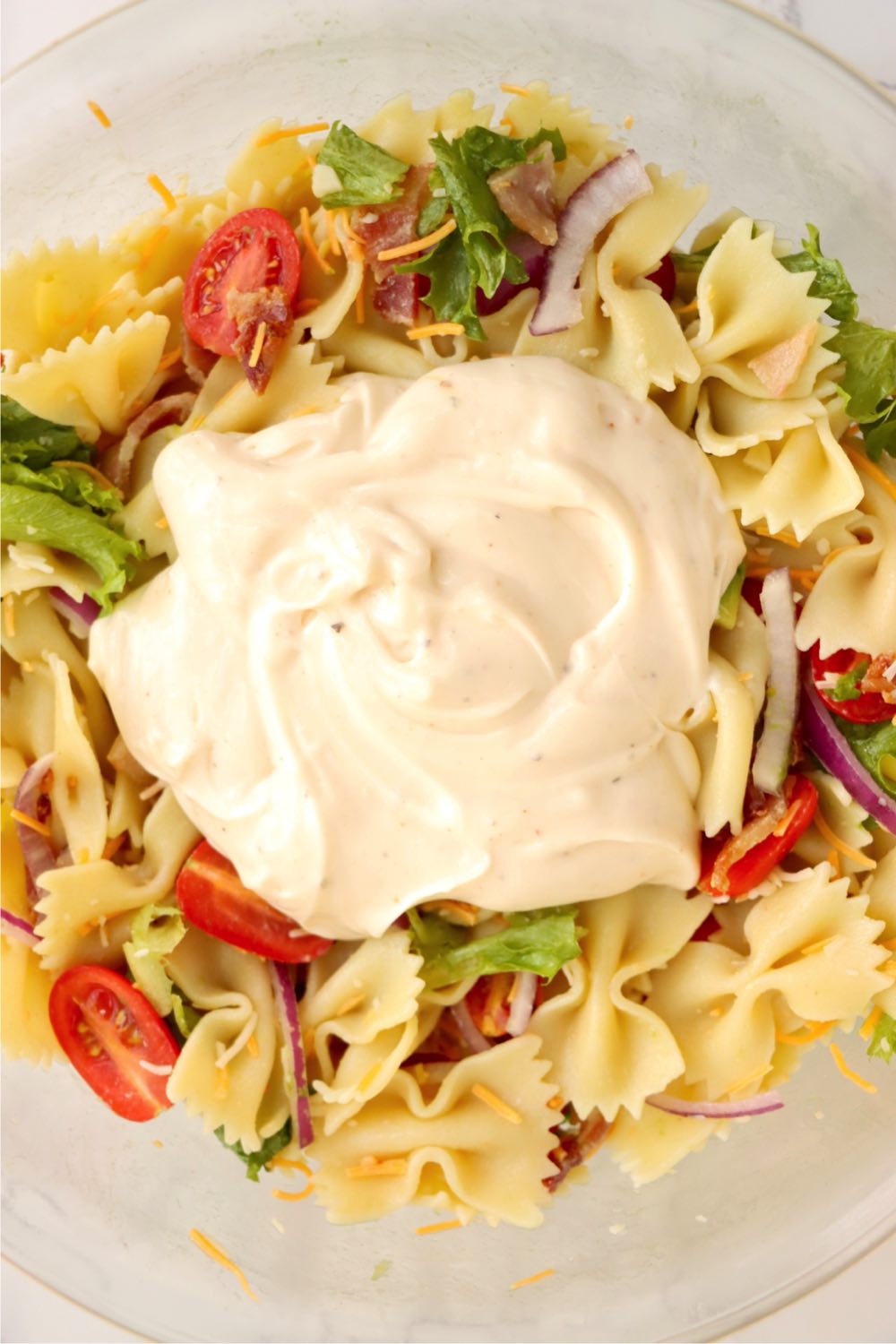 Bowl full of bowtie pasta salad topped with a big dollop of ranch dressing.