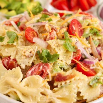 White bowl filled with bowtie pasta salad, lettuce, tomatoes and bacon.
