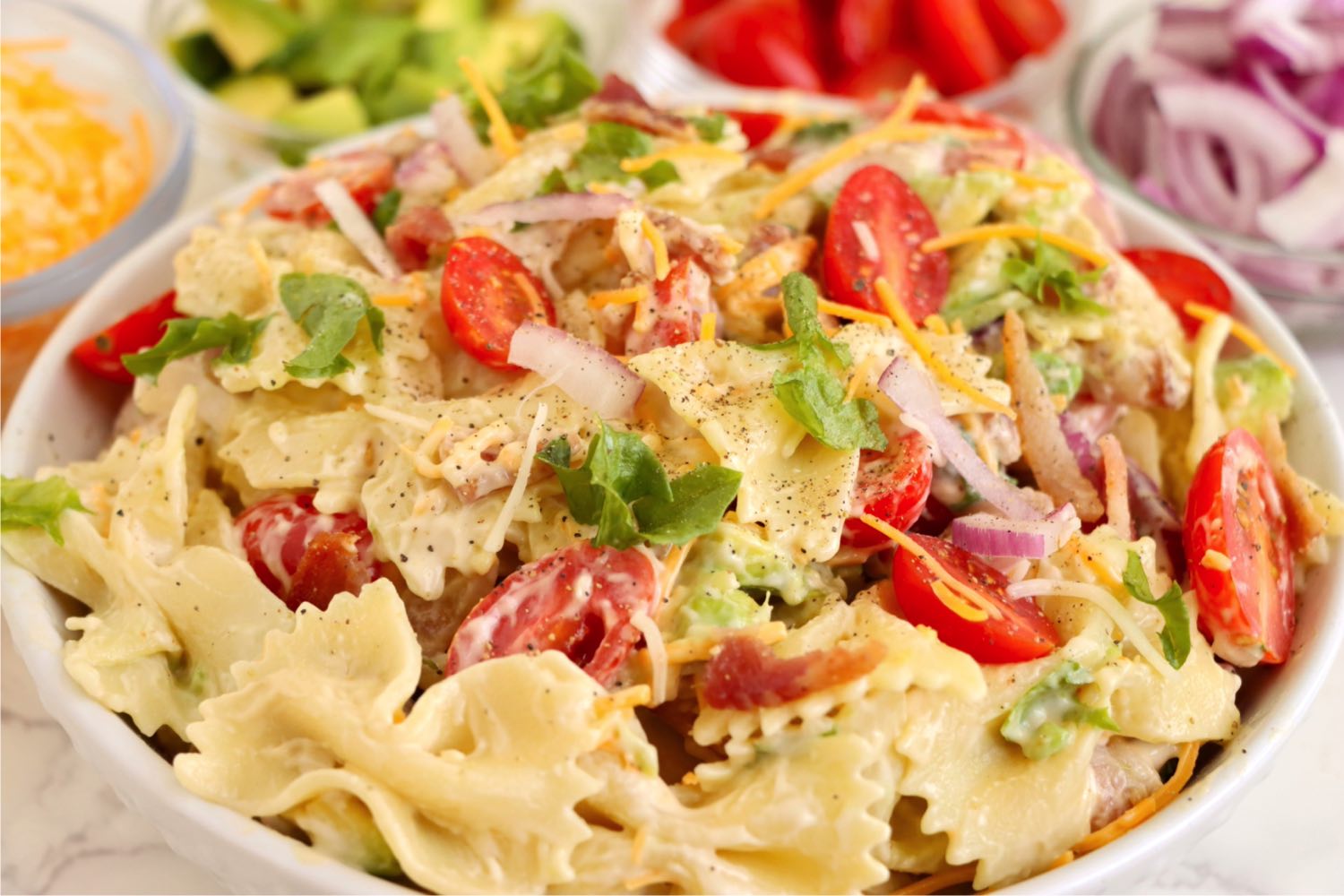 White bowl filled with bowtie pasta salad, lettuce, tomatoes and bacon.