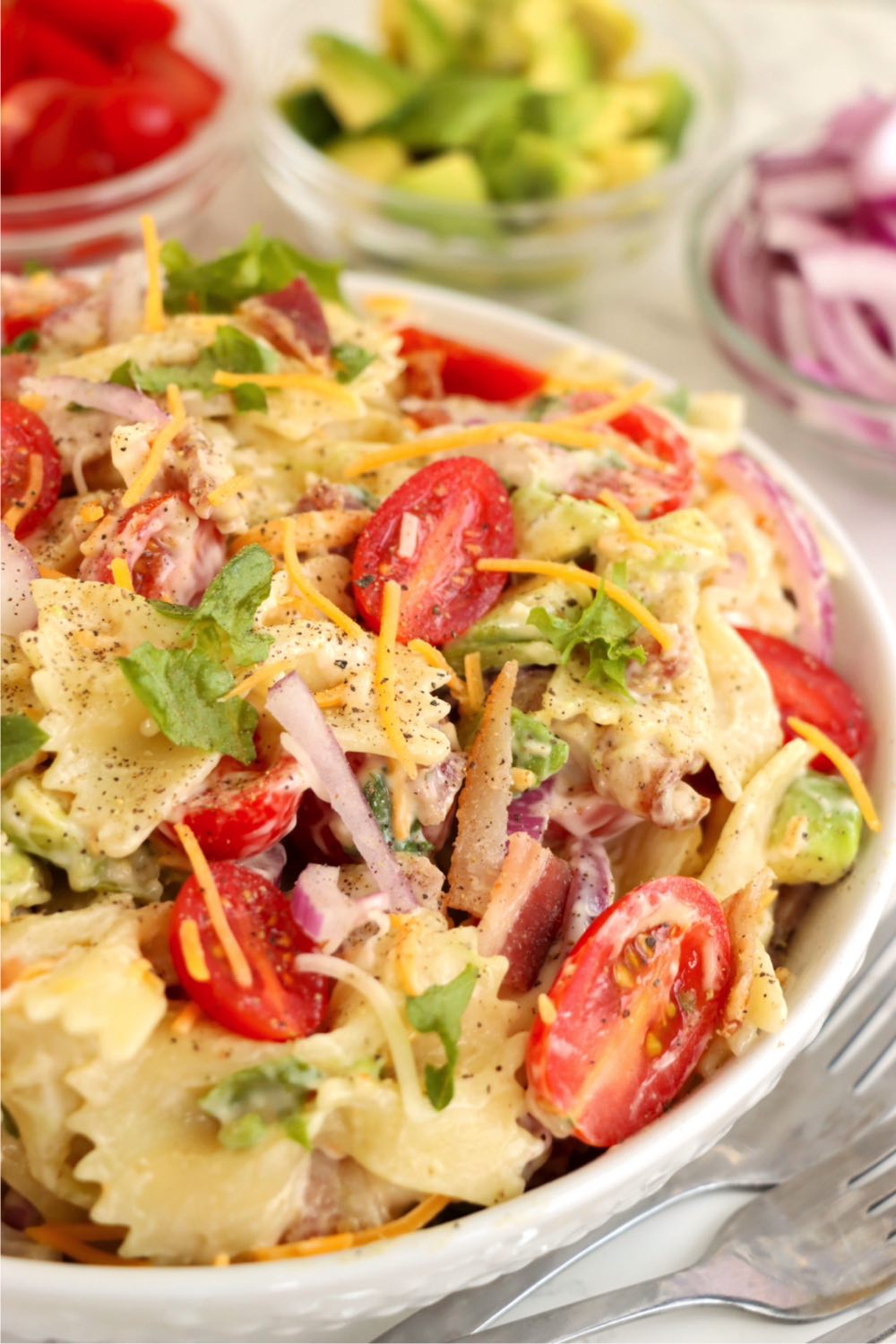 White bowl filled with bowtie pasta, lettuce, tomatoes and bacon.