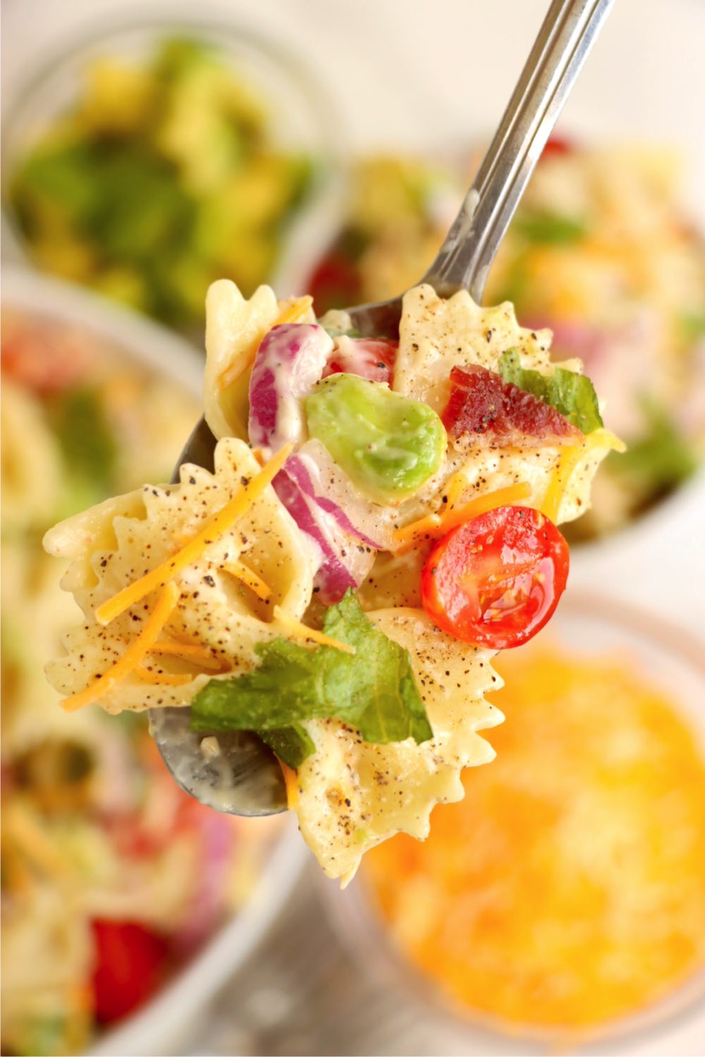 Spoonful of bowtie pasta salad with tomatoes, red onion and lettuce.