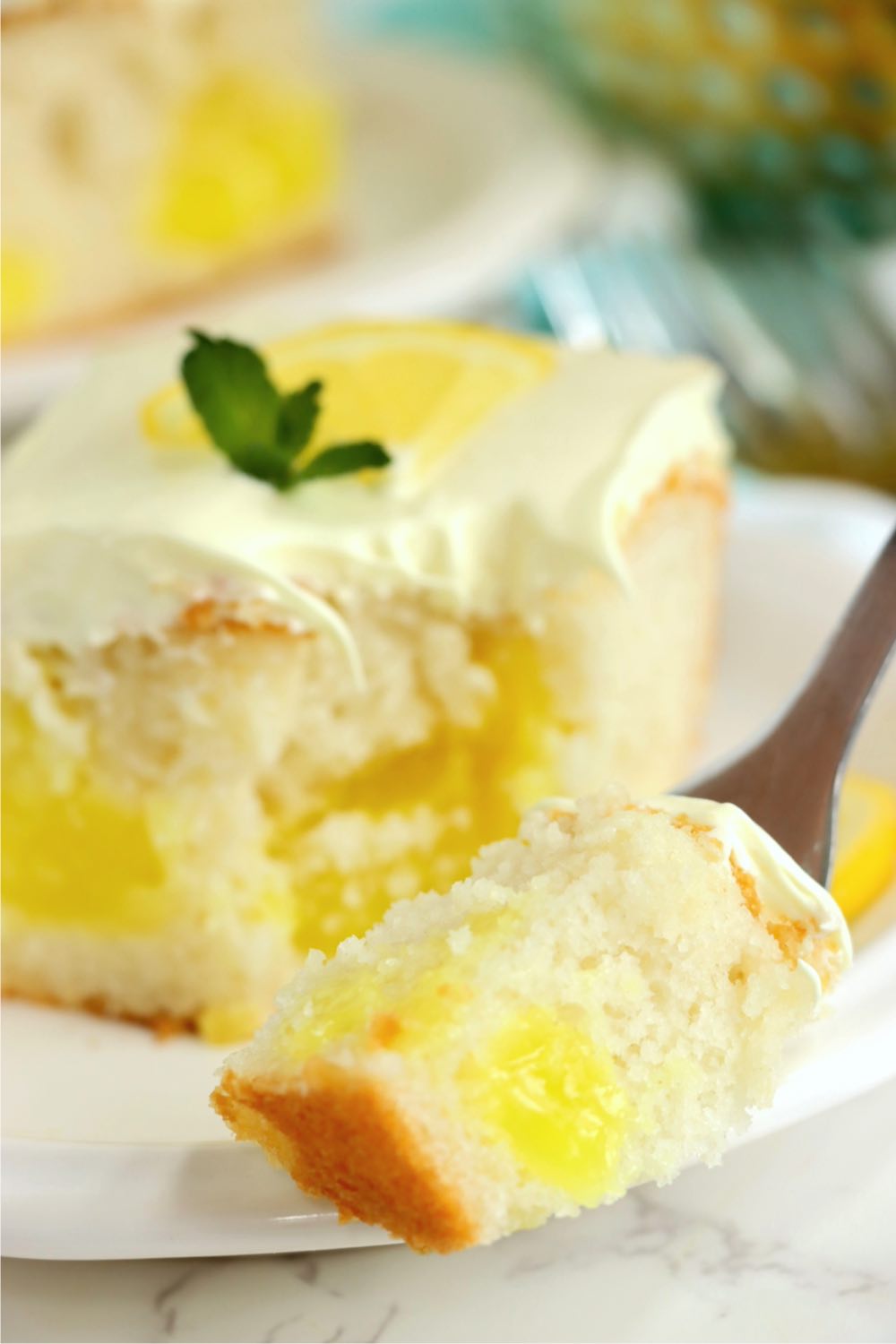 Fork filled with lemon cake in front of a piece of lemon cake.